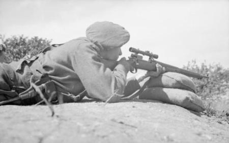 A British sniper takes aim through the telescopic sights of his rifle on the range at a sniper training school in France, 27 July 1944.
